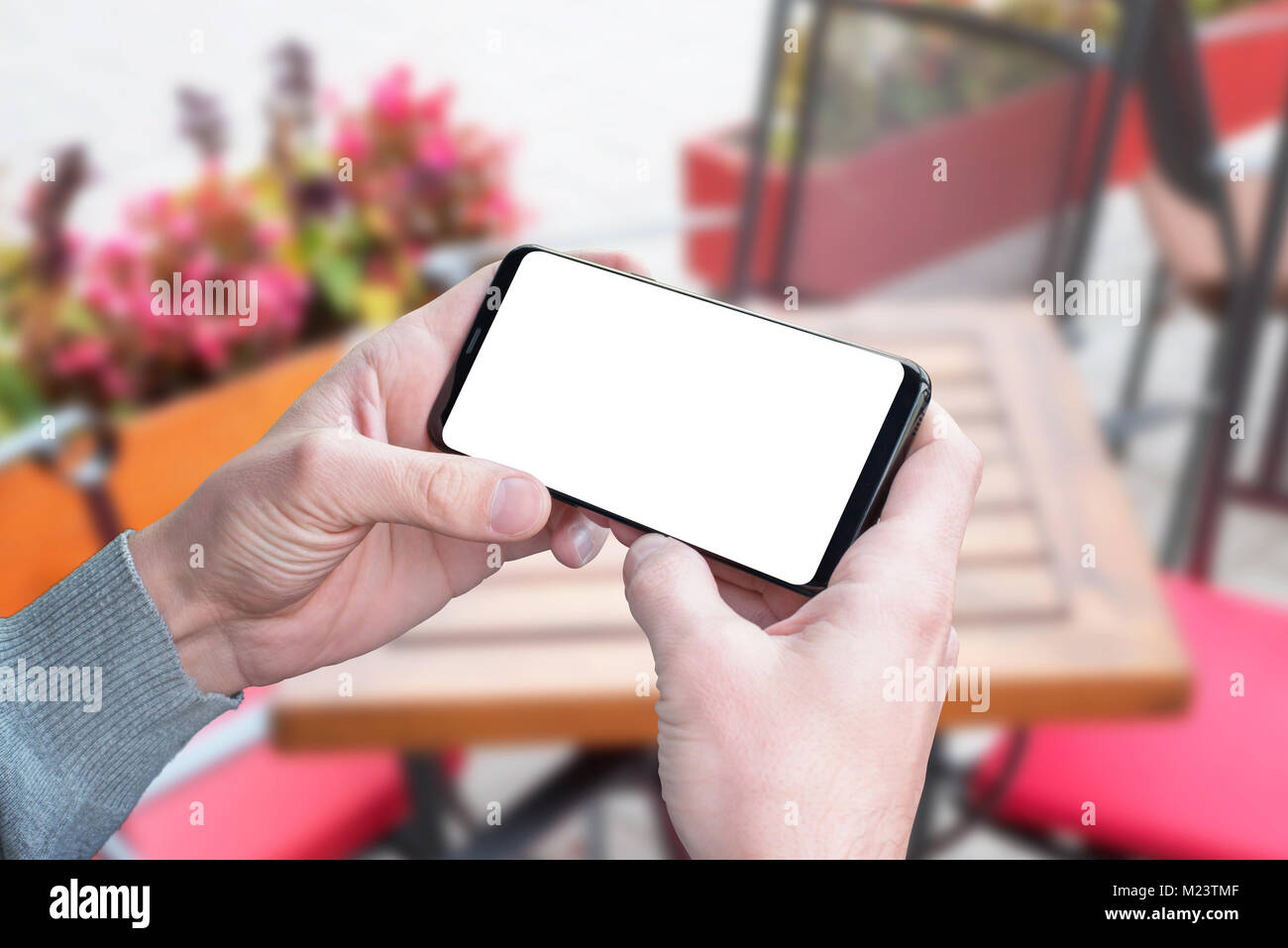 Man hold smart phone in horizontal position with isolated screen for mockup, app, video, game design presentation. Coffee shop in background. Stock Photo