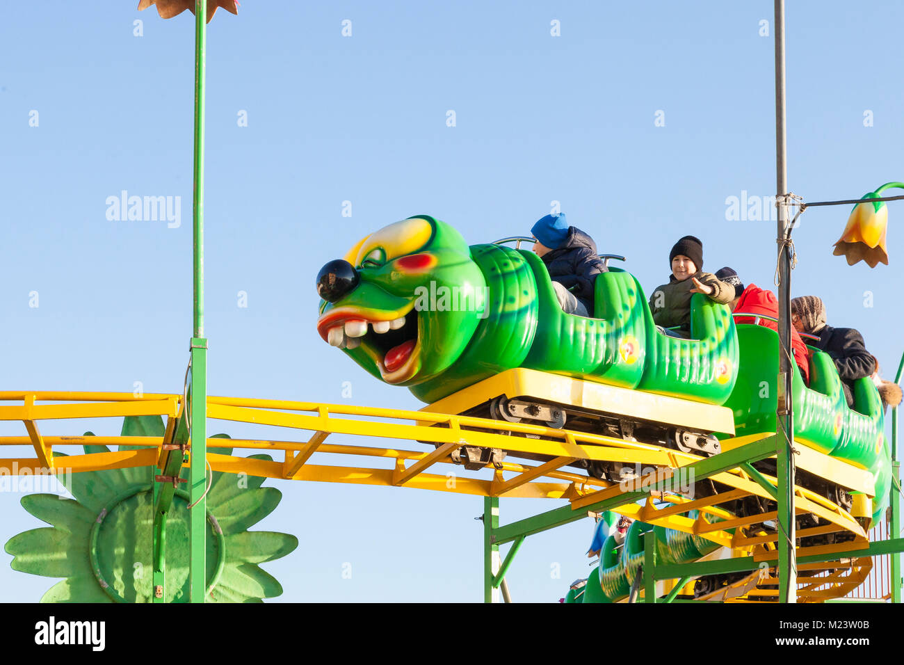 Young children and parents riding on a Wacky Worm style roller coaster at a funfair. Close up against blue sky Stock Photo