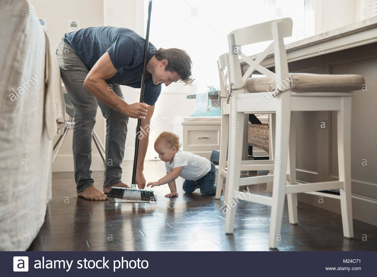 Baby son watching father sweeping floor Stock Photo