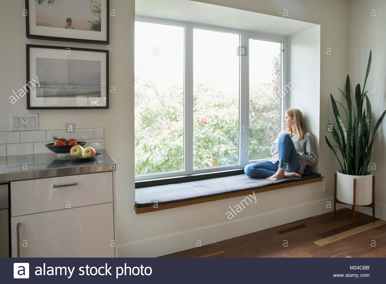 Thoughtful woman relaxing at window seat, looking out window Stock Photo