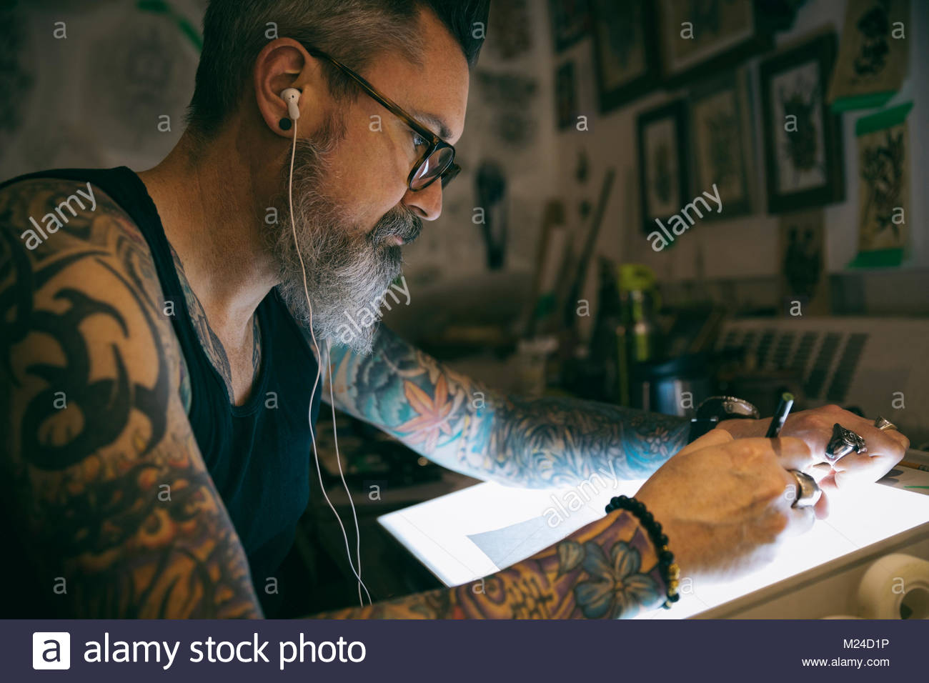 Tattoo artist listening to music and sketching at light table in dark