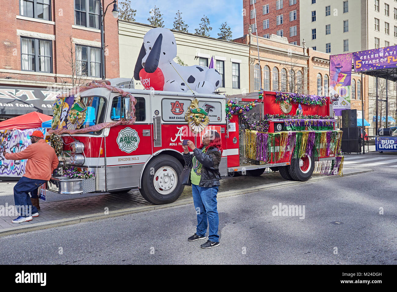 Two people taking pictures, one a selfie, at the local Mardi Gras celebration with a decorated fire truck in background in Montgomelry Alabama, USA. Stock Photo