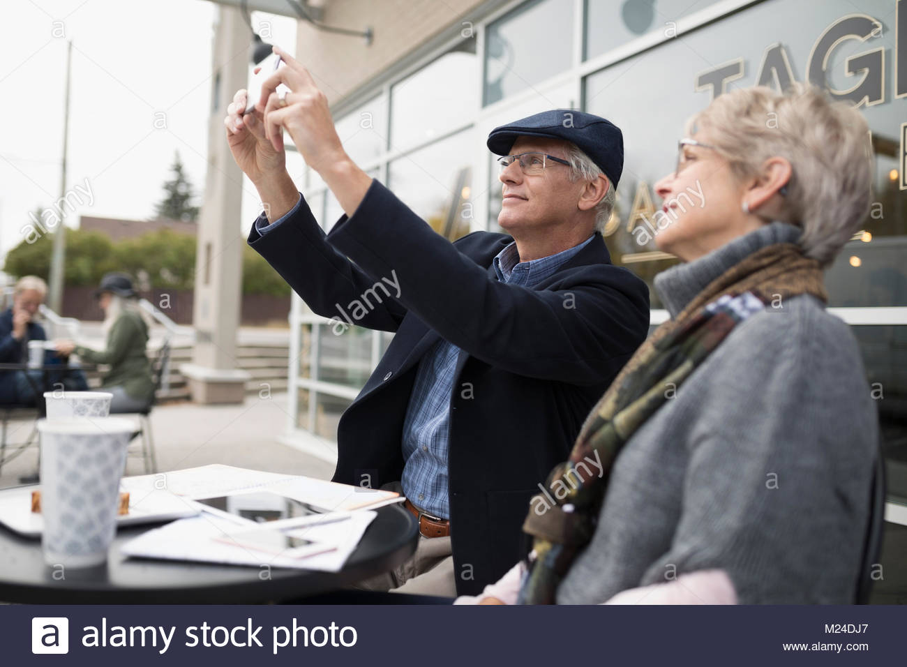 Senior couple using camera phone at sidewalk cafe Stock Photo