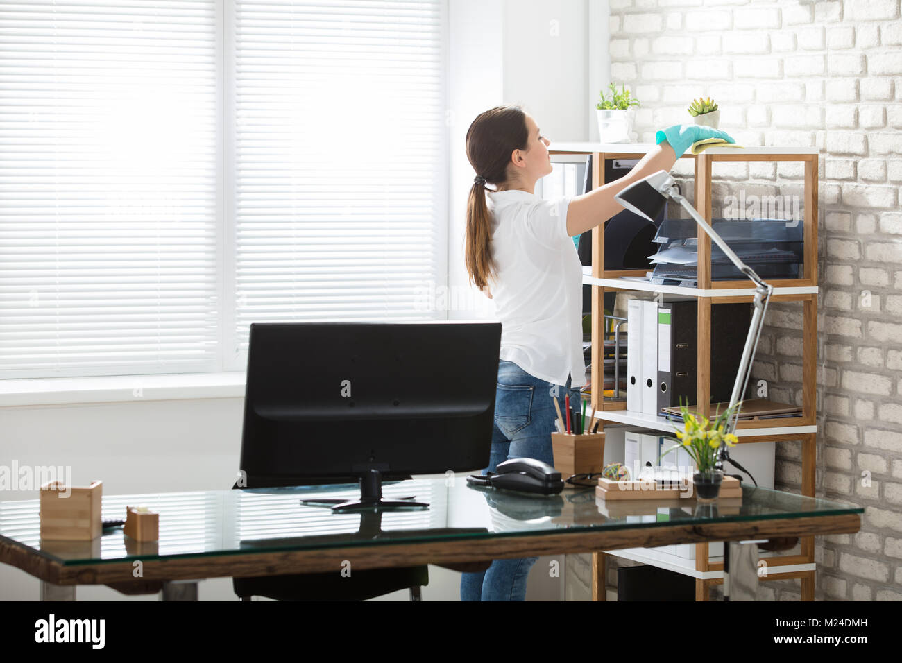 Young Woman Cleaning The Shelves With Rag In Modern Office Stock Photo