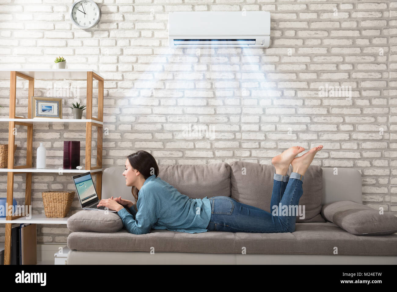 Woman Lying On Sofa Using Laptop Enjoying The Cooling Of Air Conditioner At  Home Stock Photo - Alamy