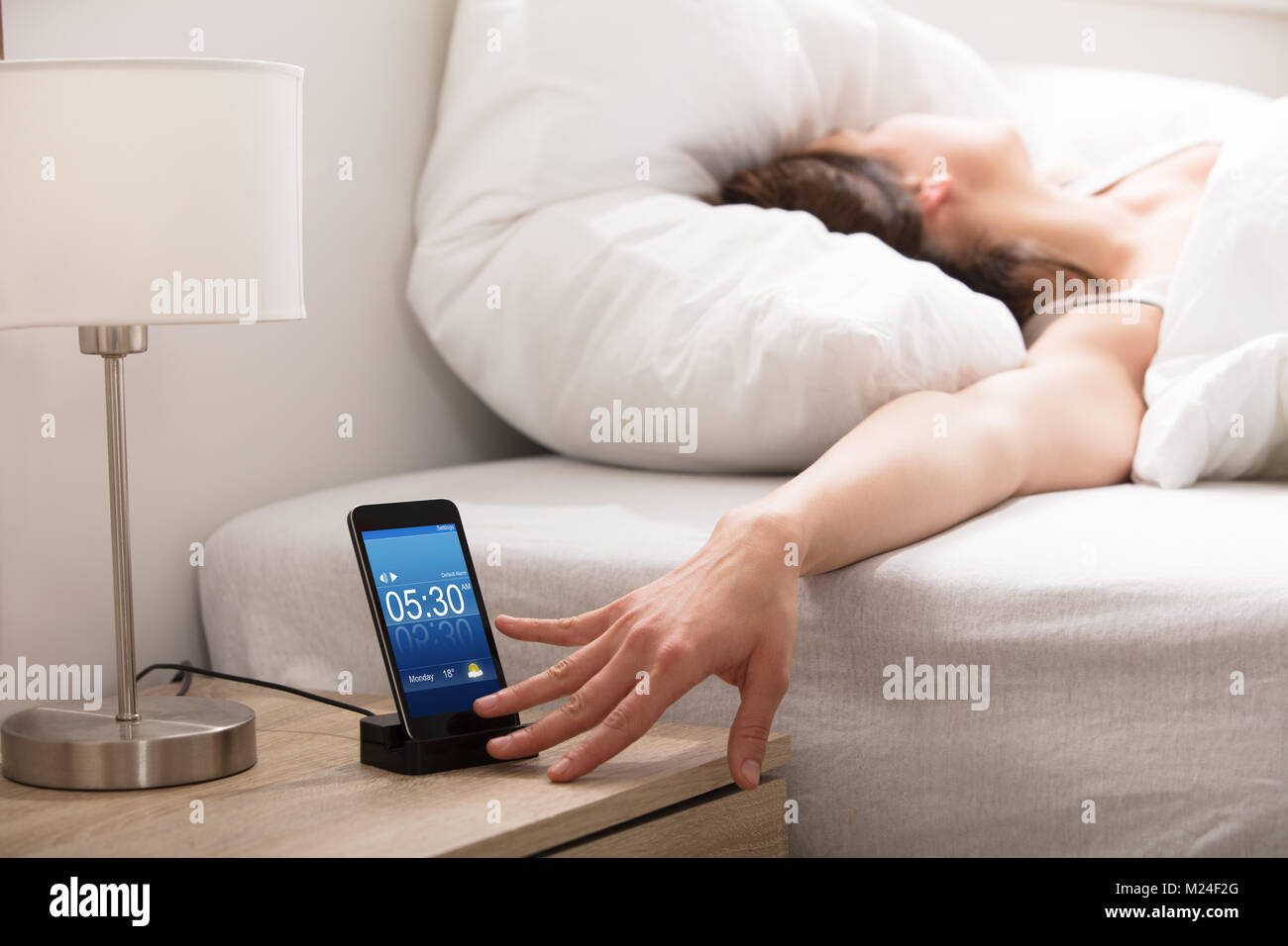 Woman Turning Off The Alarm On Cell Phone While Waking Up In The Morning Stock Photo