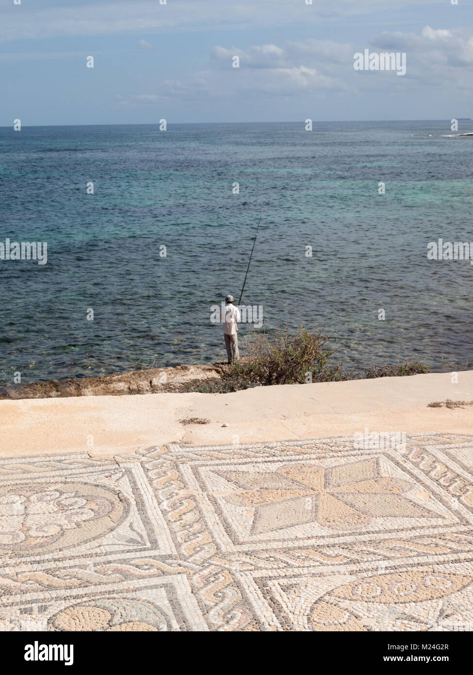 Mosaic of the Roman ruins of the Baths of Oceanus in Sabratha with sea and fisherman in background Stock Photo