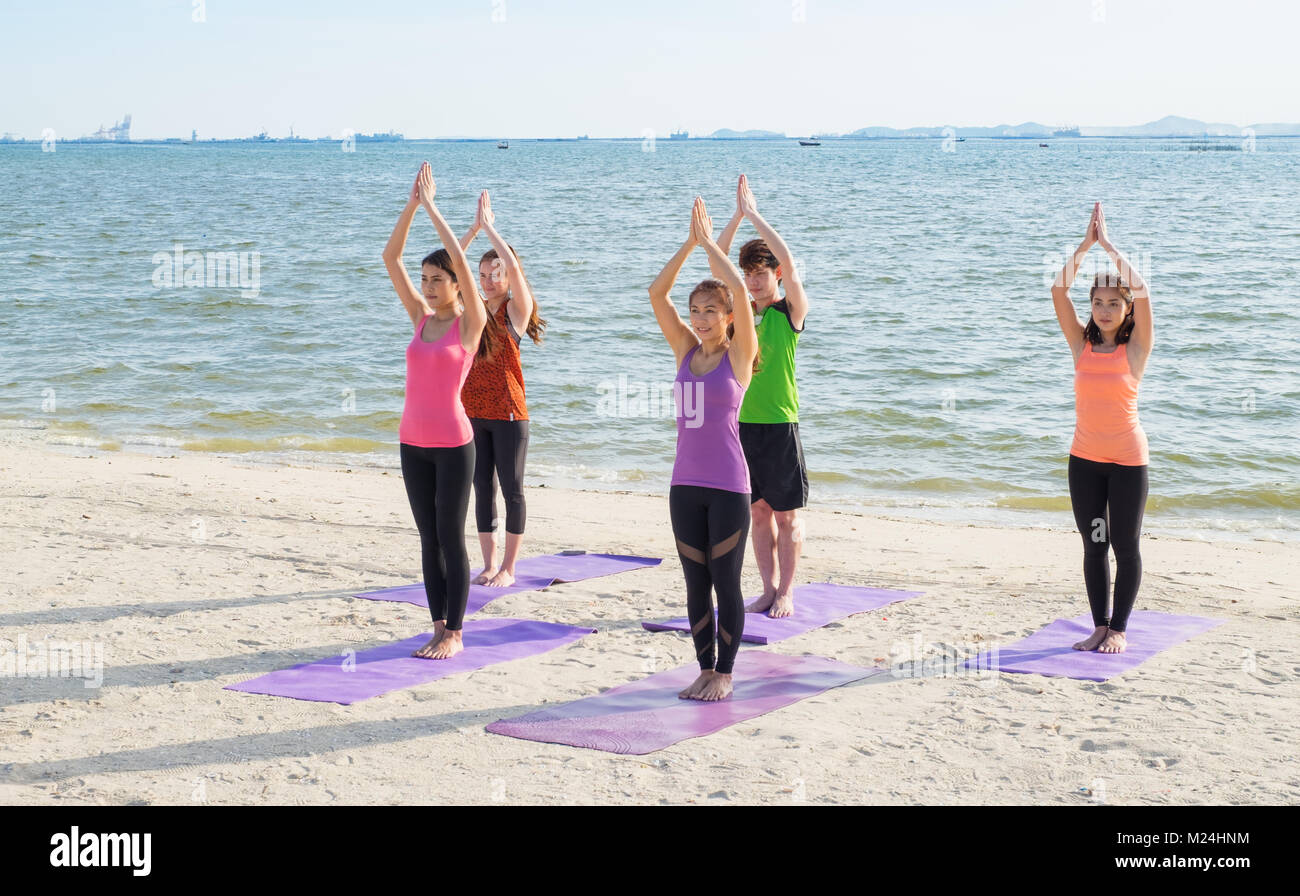 Yoga class at sea beach in evening ,Group of people doing namaste poses with clam relax emotion at beach,Meditation pose,Wellness and Healthy balance  Stock Photo