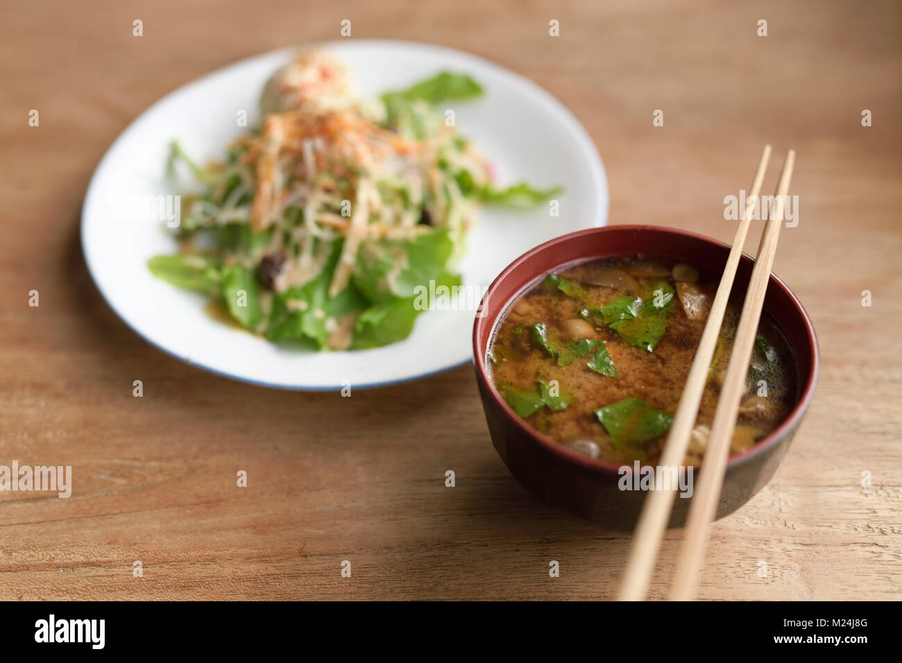 A bowl of spicy Miso soup and a plate of vegetable salad in a Japanese vegan restaurant, food still life on a wooden table. Kyoto, Japan. Stock Photo