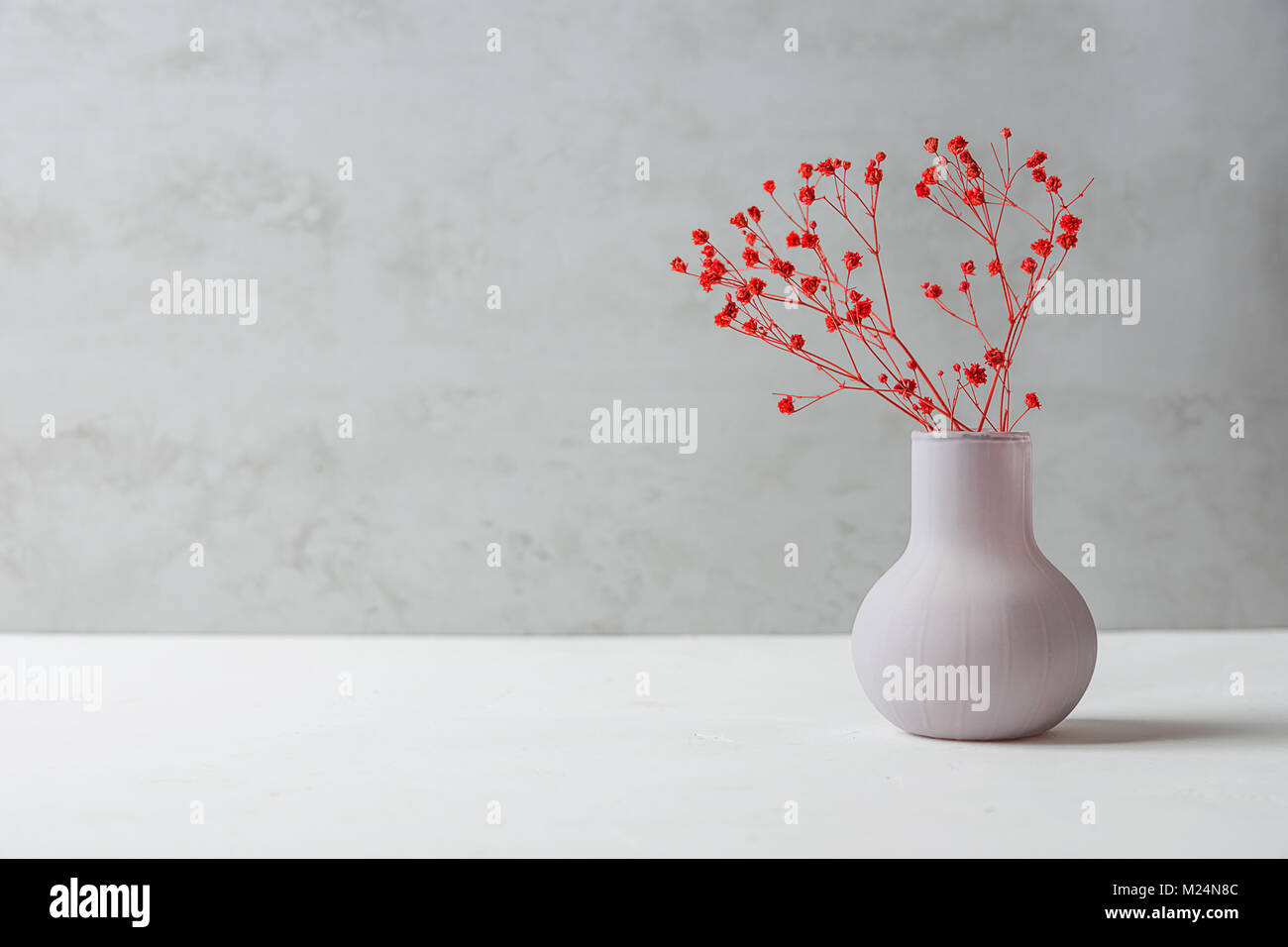 Small Bouquet of Red Flowers in Vintage Vase on White Table Grey Cement Wall Background. Styled Stock Image Mockup for Text Artwork Quotes Lettering W Stock Photo