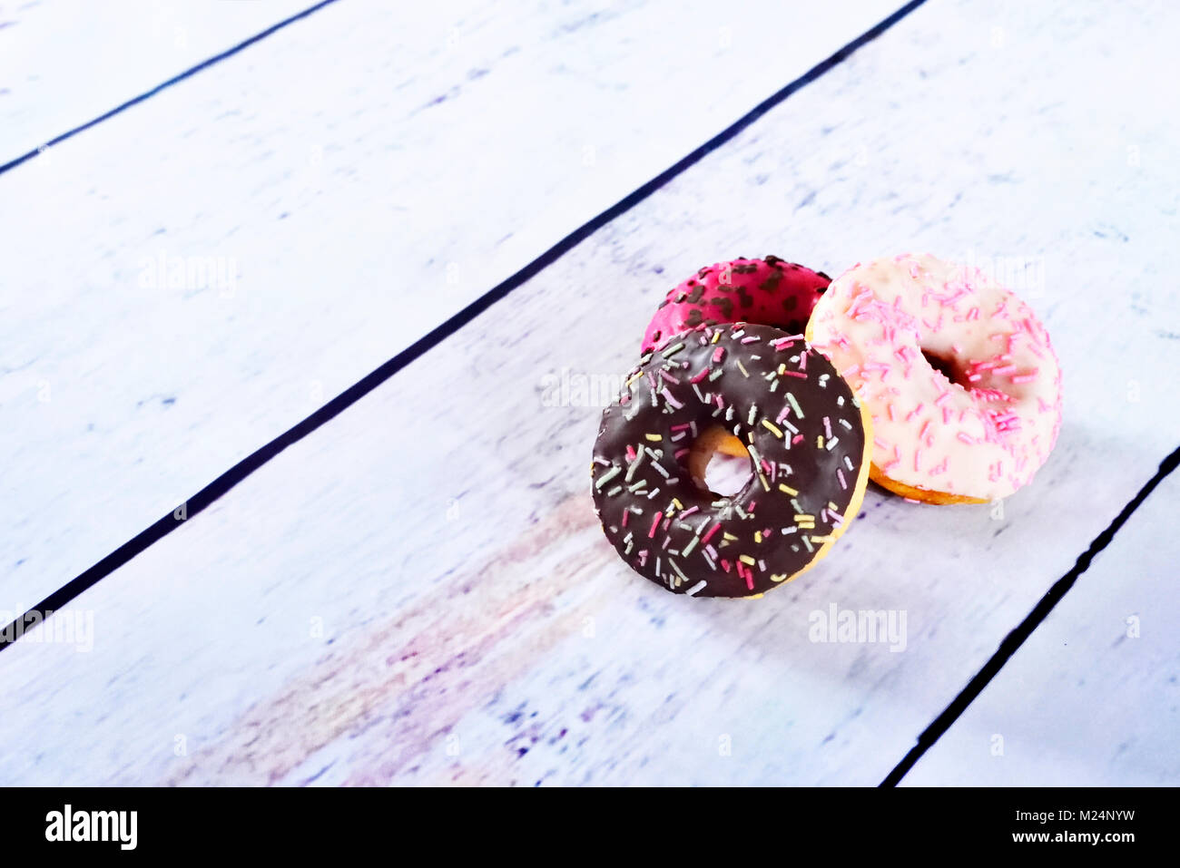 delicious donuts with glaze or icing and sprinkles. variation of fresh donuts on a white wooden table. Arrangement with copy space. Stock Photo