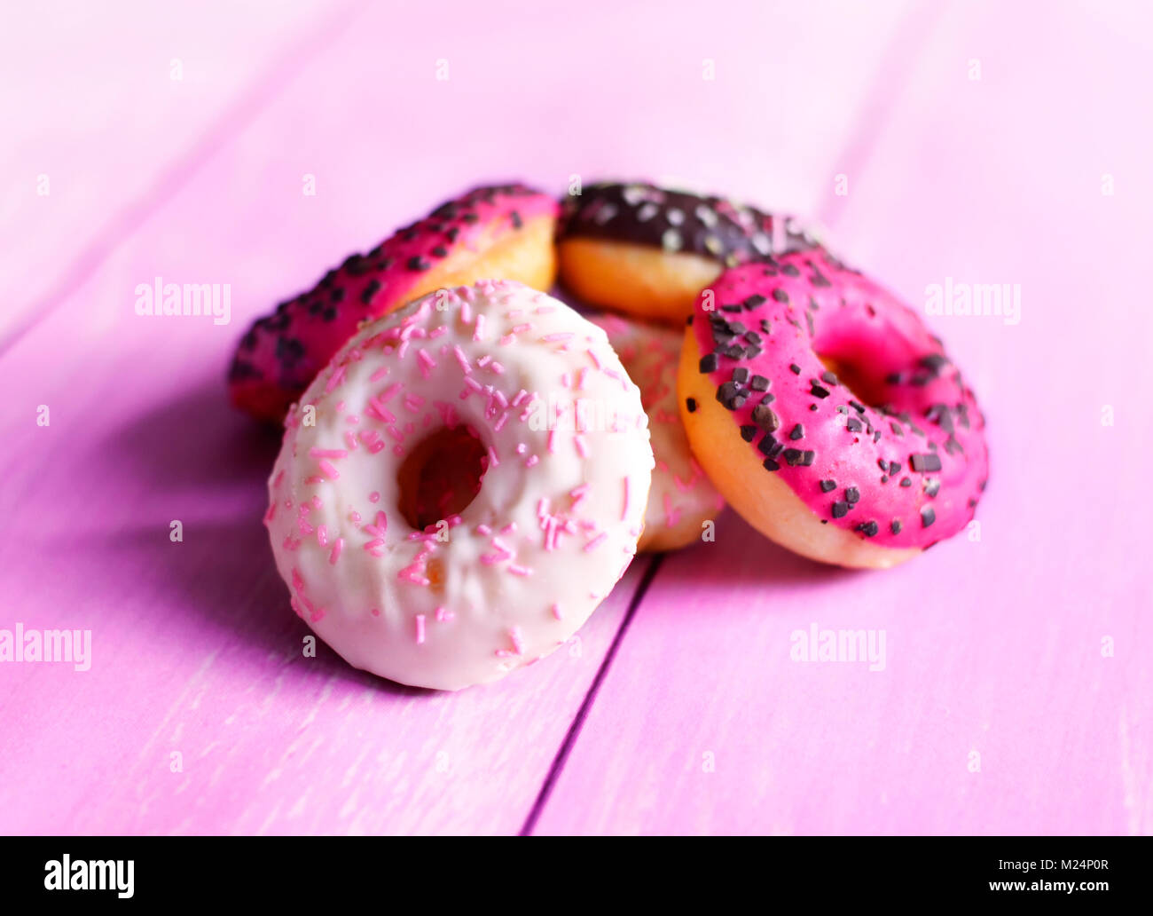 Delicious glazed donuts with sprinkles. Pink table and arrangement of chocolate donuts, various donuts, sweet food or unhealthy eating scene. Stock Photo