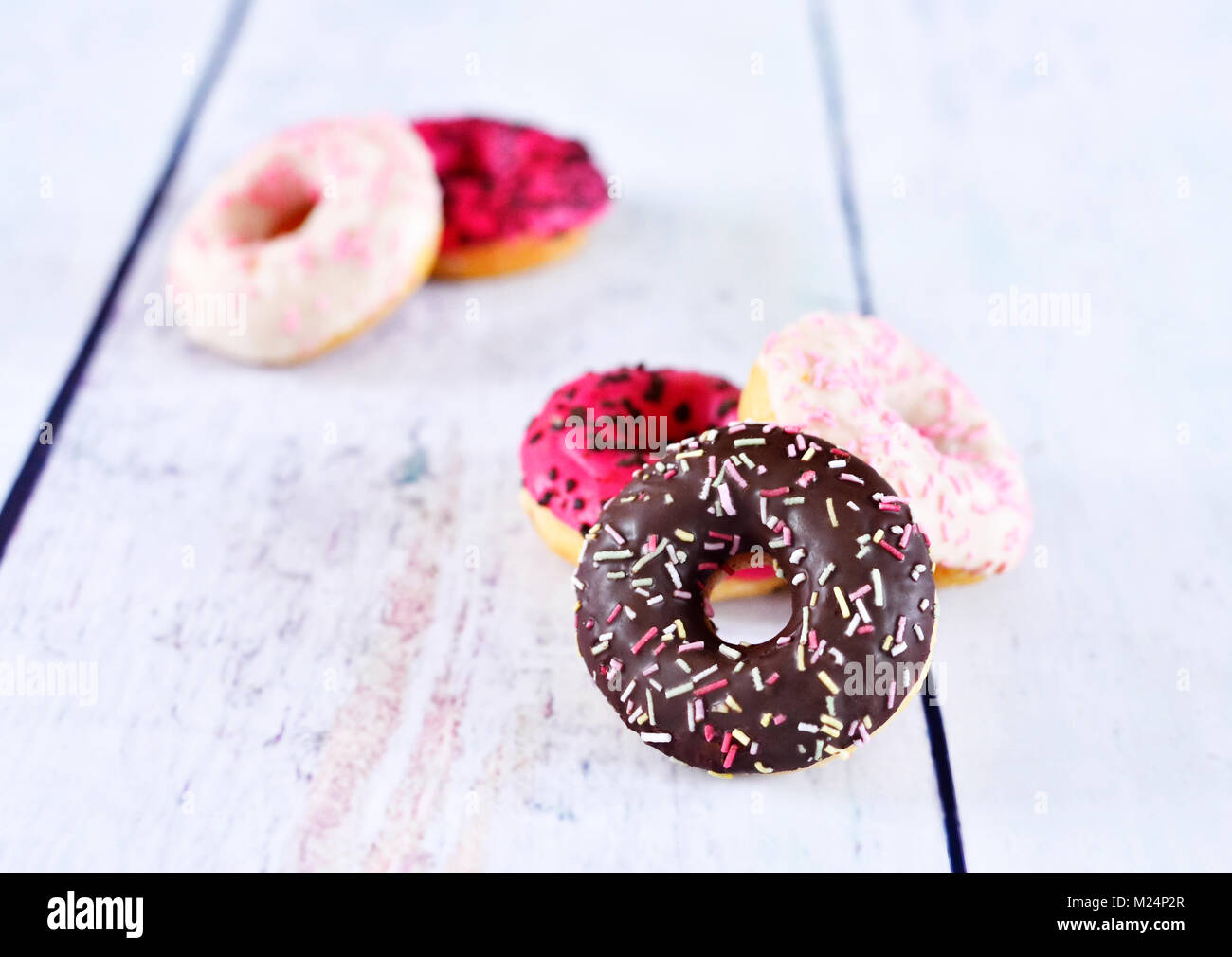 delicious donuts with glaze or icing and sprinkles. variation of fresh donuts on a white wooden table. Arrangement with copy space. Stock Photo