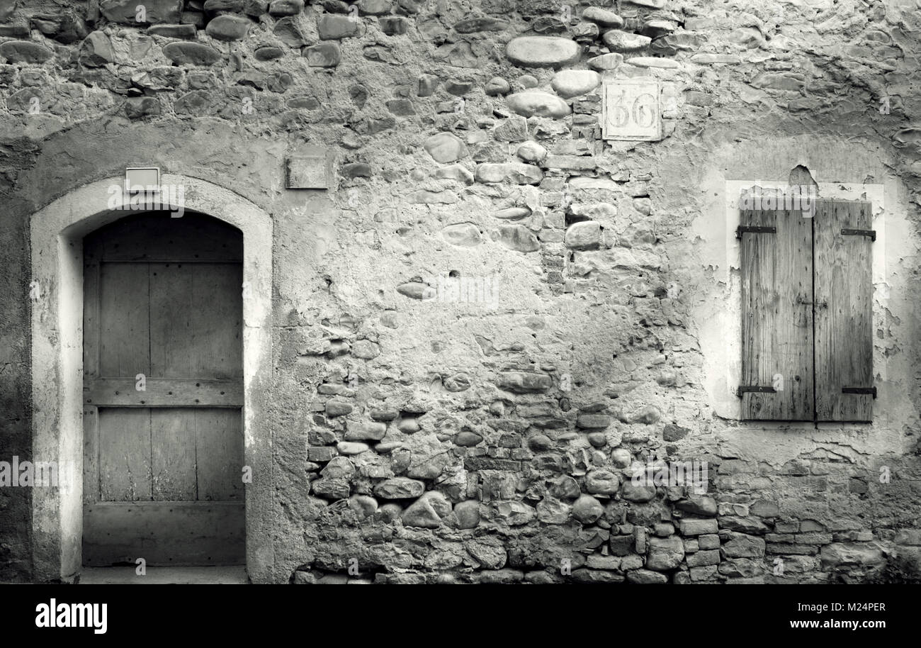 Old stone wall with door and window with closed shutters in black and ...