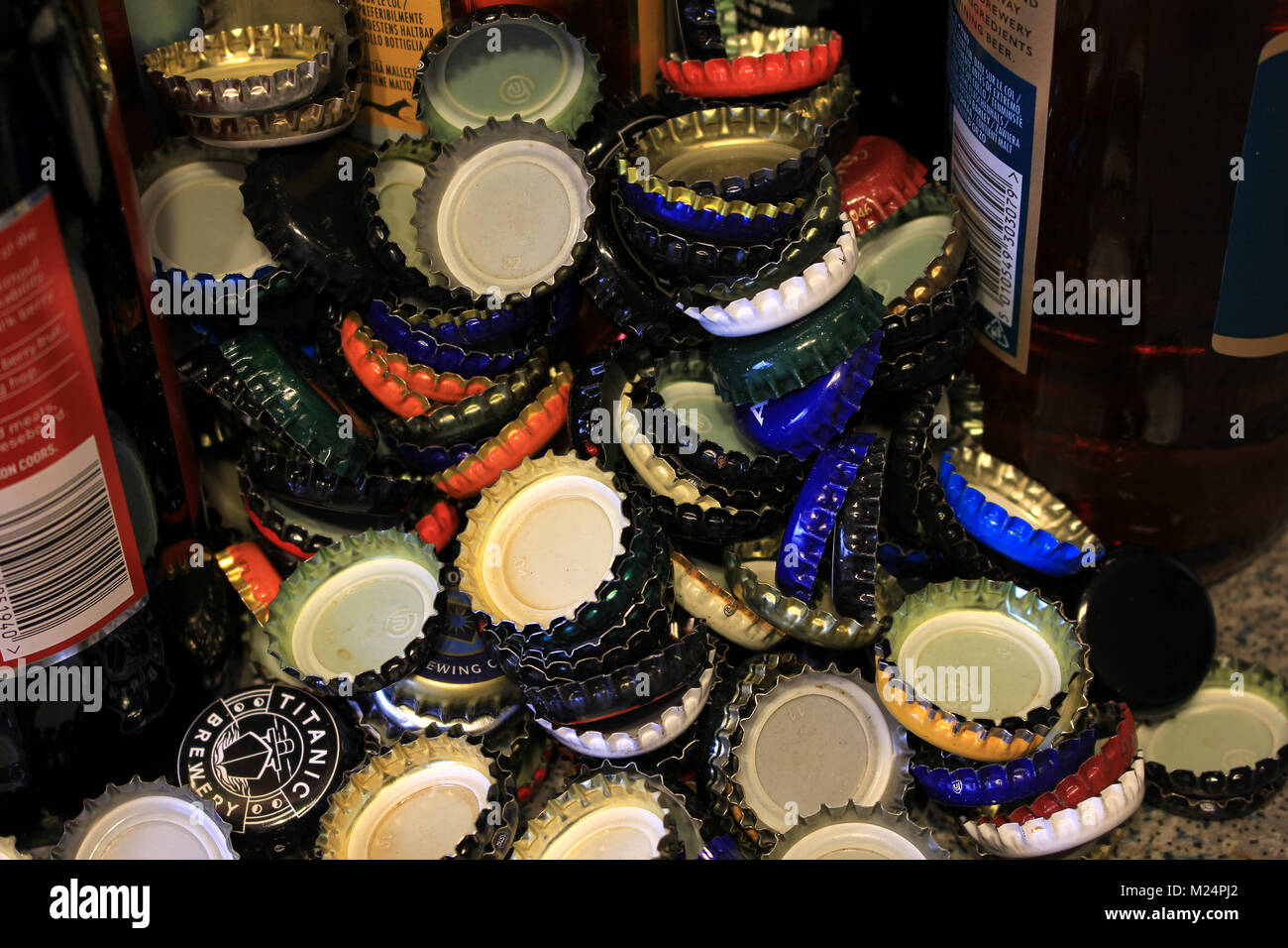 Used beer bottle tops have been collected and are piled up against some beer bottles yet to be emptied. Stock Photo