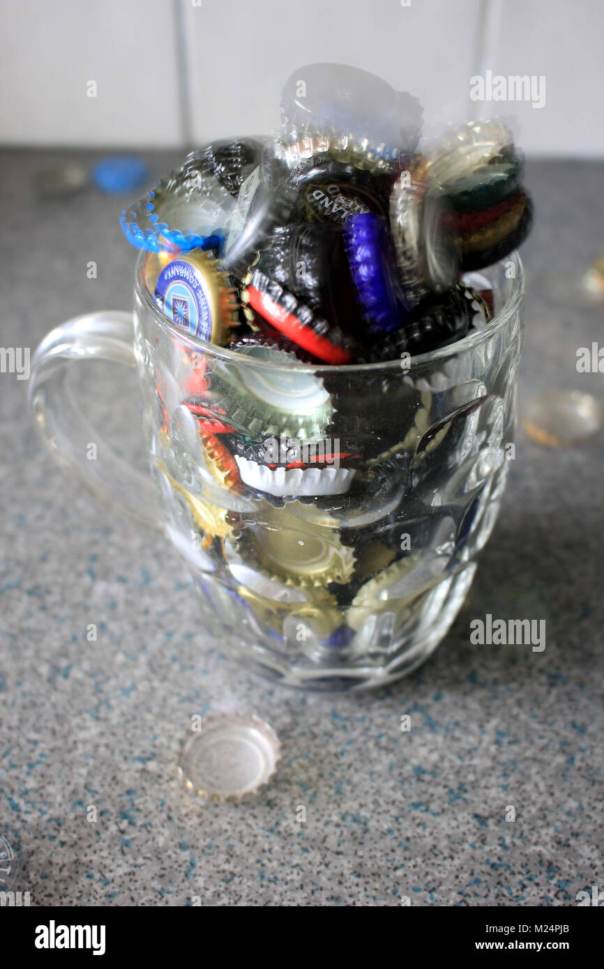 Used beer bottle tops have been collected and are over flowing from a pint jug with a few ghostly ones floating about as well. Stock Photo