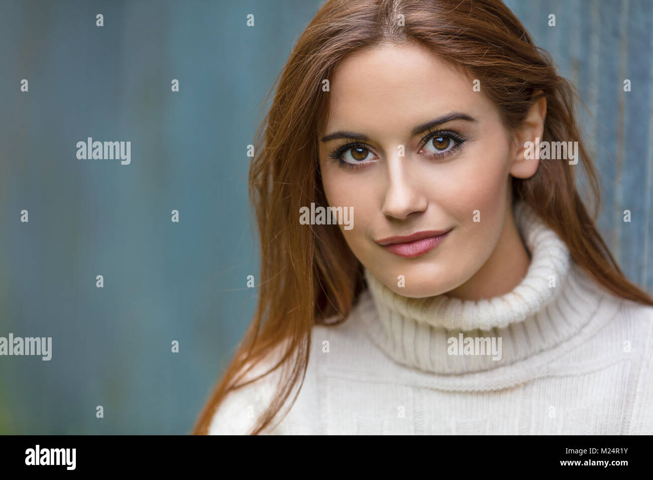 Outdoor portrait of beautiful girl or young woman with red hair wearing a white jumper Stock Photo