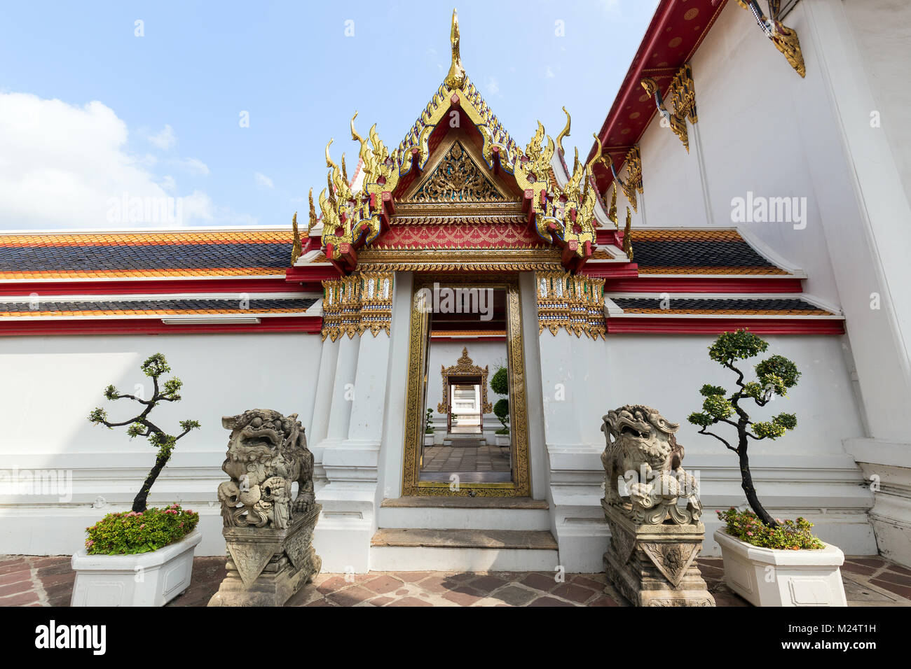 Two statues in front of a decorated and open door and gate at the Wat Pho (Po) temple complex in Bangkok, Thailand, on a sunny day. Stock Photo