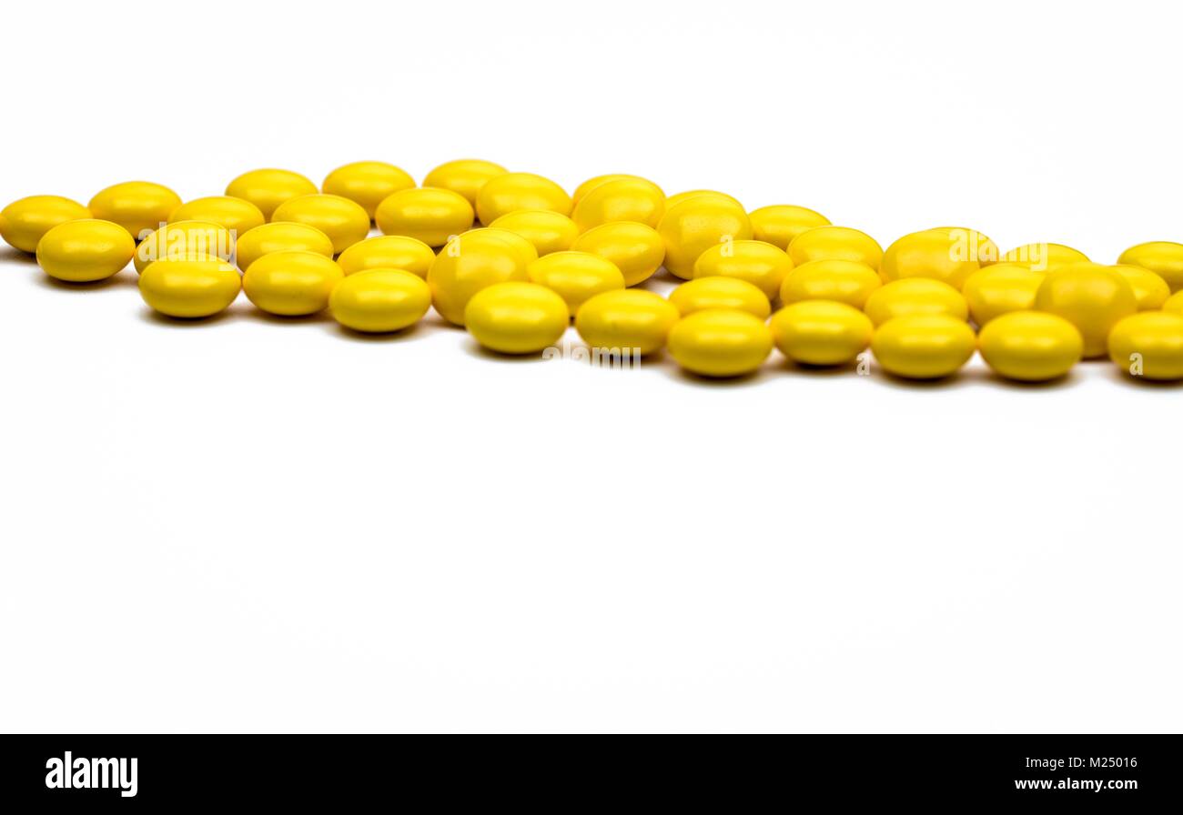 Macro shot detail of yellow round sugar coated tablets pills on white background with copy space for text. Stock Photo