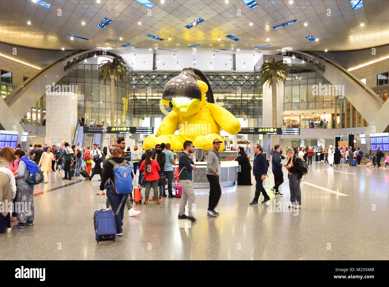 Qatar, Doha, Hamad International Airport. Within the transit area, the crowd move around the main lobby where the iconic giant lamp bear is located. Stock Photo