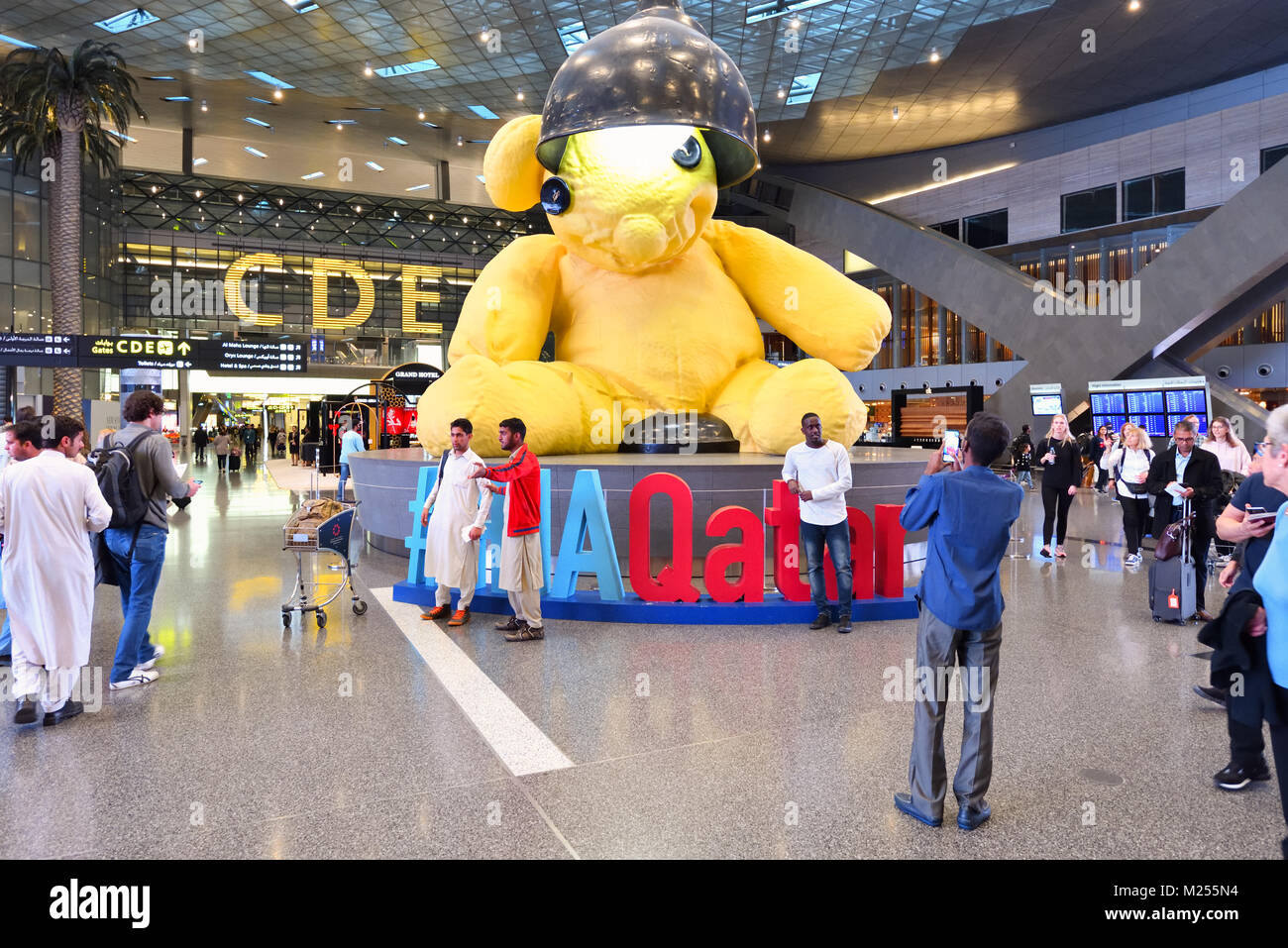Qatar, Doha, Hamad International Airport. Within the transit area at the main lobby, visitors gather around the giant lamp bear for pictures. Stock Photo