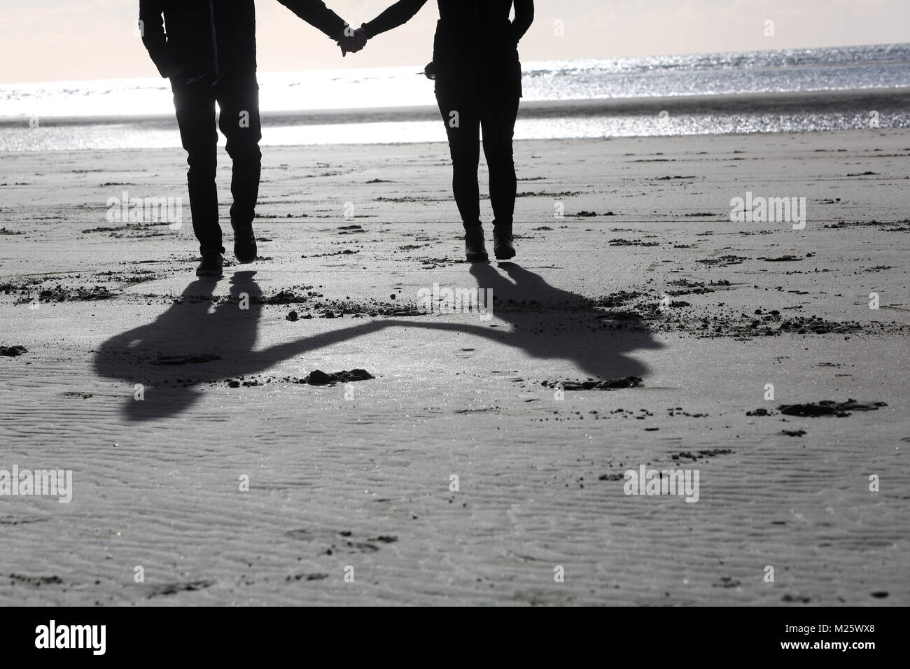 Silhouette of a couple holding hands on beach at sunset hi-res stock ...