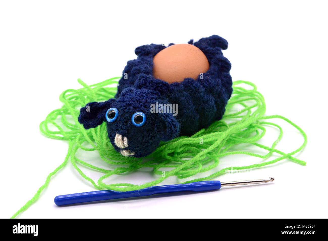 crochet blue Easter lamb egg cup made of wool with crochet hook, white isolated background Stock Photo