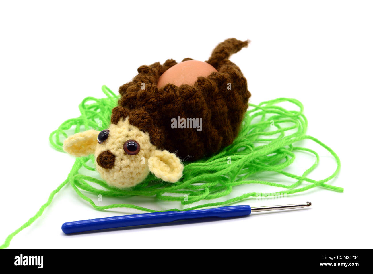 crochet brown Easter lamb egg cup made of wool with crochet hook, white isolated background Stock Photo