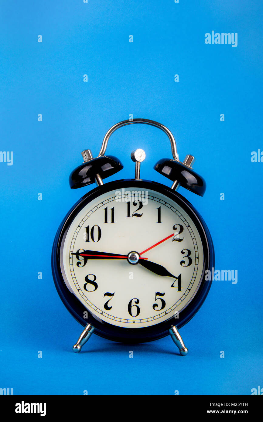 Black alarm clock with a blue background showing time Stock Photo - Alamy