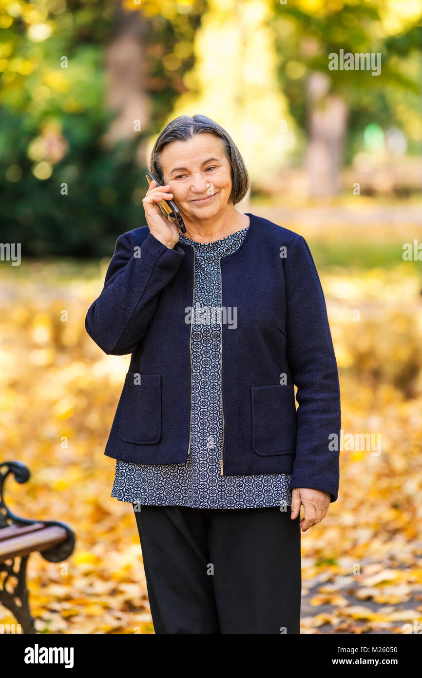 Positive senior woman talking on smartphone outdoors in park. Stock Photo