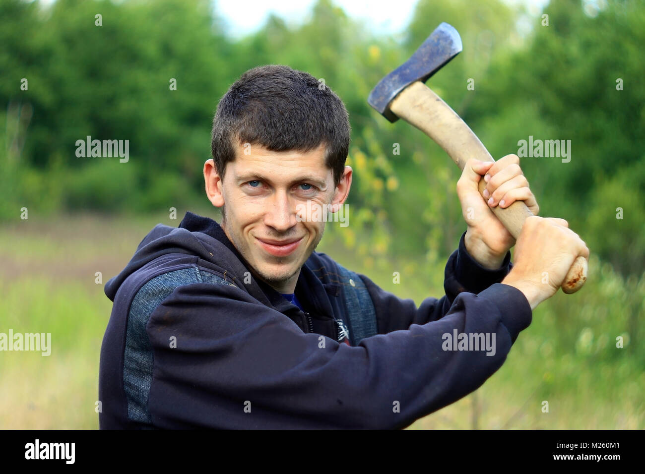 Young man with an axe chopping someone in summer forest Stock Photo