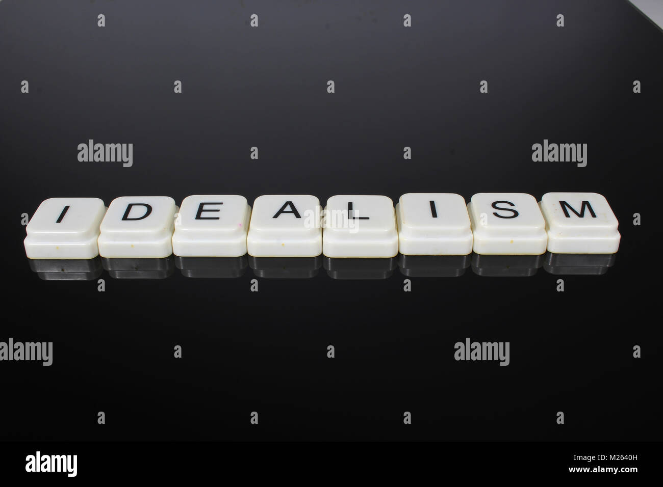 Idealism text word title caption label cover backdrop background. Alphabet letter toy blocks on black reflective background. White alphabetical letter Stock Photo