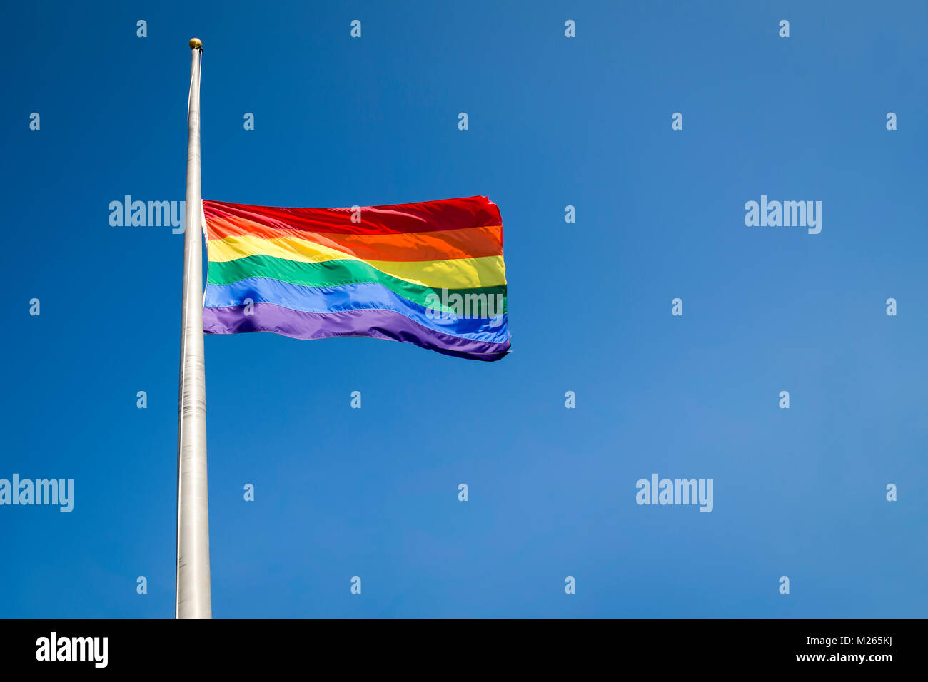 Gay pride rainbow flag flying at half mast in mourning on bright summer