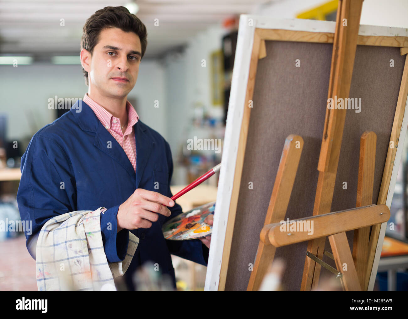 Smiling man with brush near easel painting on canvas Stock Photo - Alamy