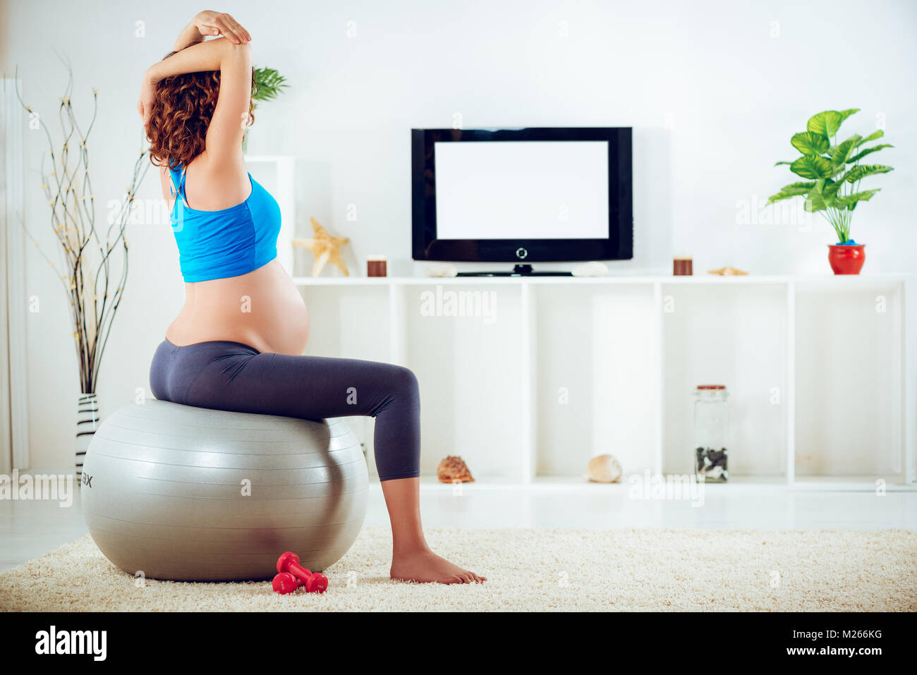 Beautiful young pregnant woman sitting on a fitness ball and doing breathing exercises. Stock Photo