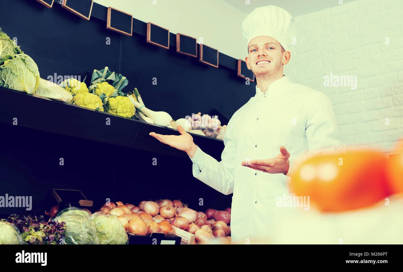 Smiling male chef looking for fresh vegetables at the grocery shop ...