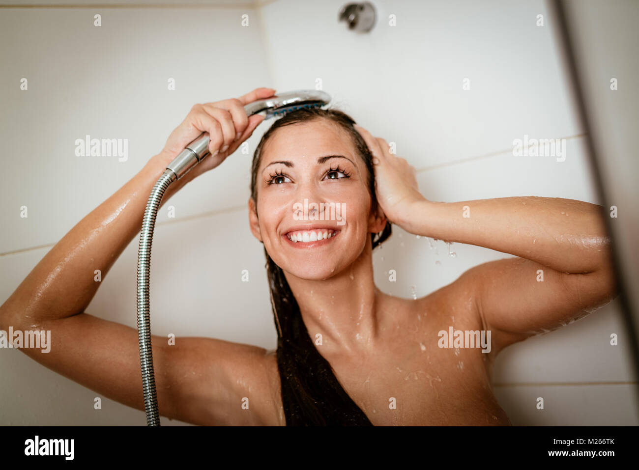 Happy young woman wetting her hair while showering under shower head. Stock Photo