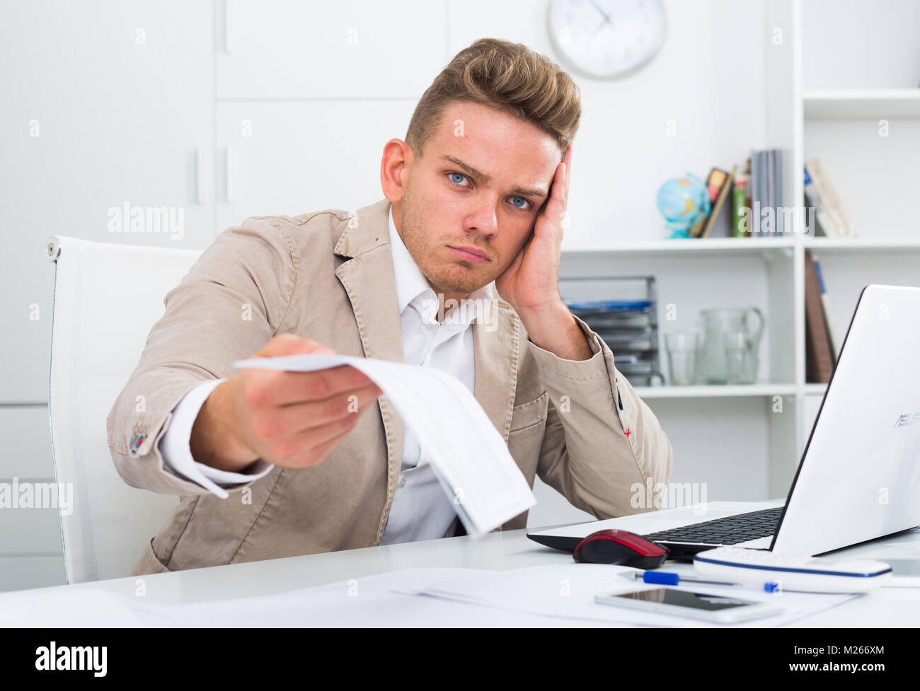 Frustrated young man having business problems with papers at workplace ...