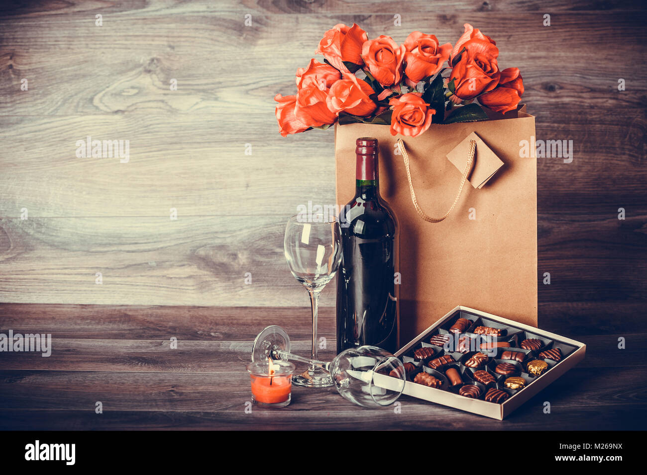 Red wine bottle, box of chocolates, roses in a paper bag on wooden ...