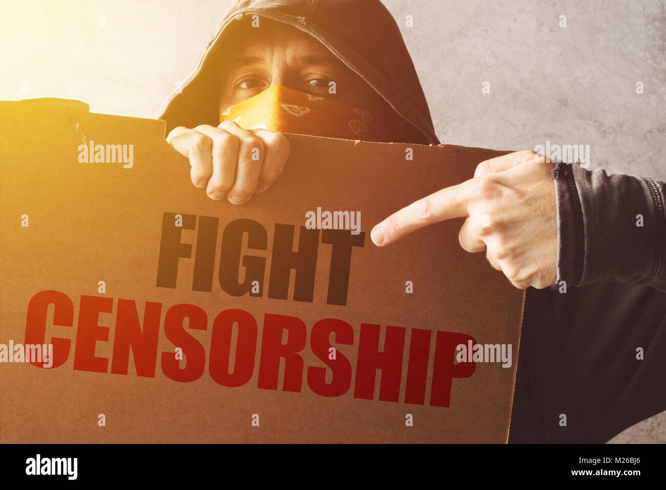 Hooded activist protestor holding Fight censorship protest sign. Man with hoodie and scarf over face taking part in activism and fighting for the caus Stock Photo