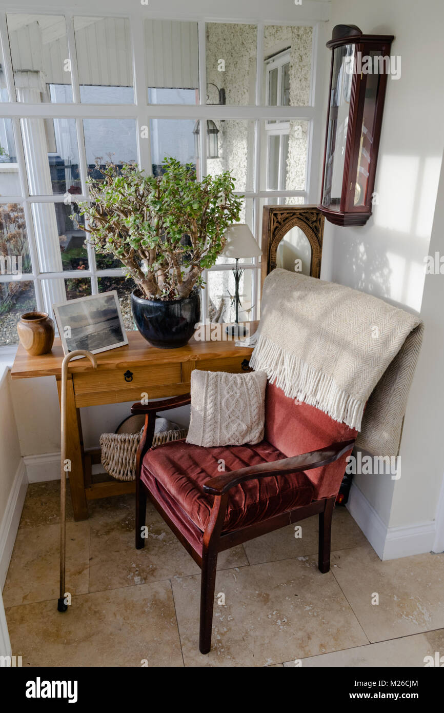 Empty comfortable red chair on a porch.Walking stick resting against a table with a plant and picture on it. Blanket is draped over the back Stock Photo