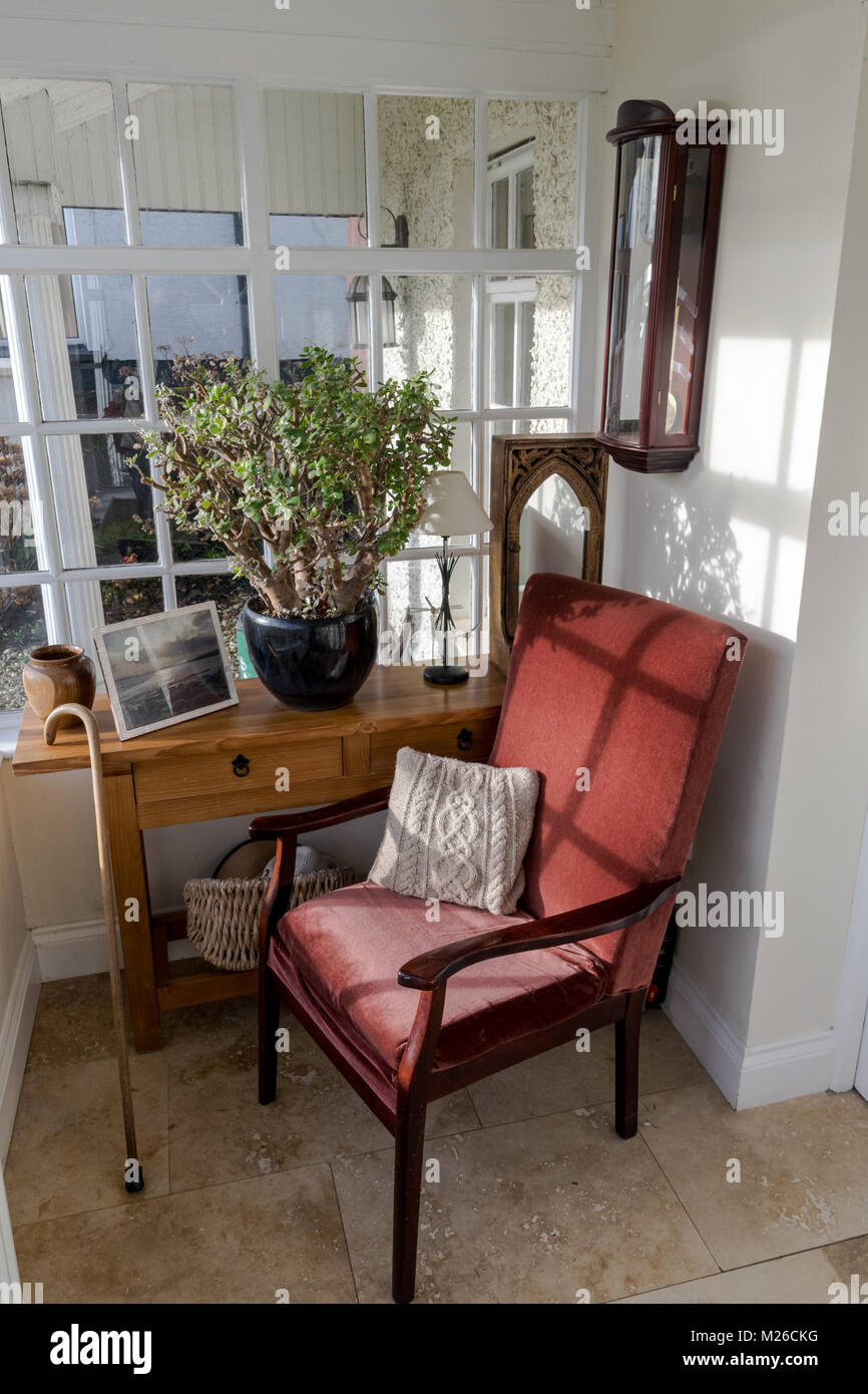 Empty comfortable red chair on a porch.Walking stick resting against a table with a plant and picture on it Stock Photo