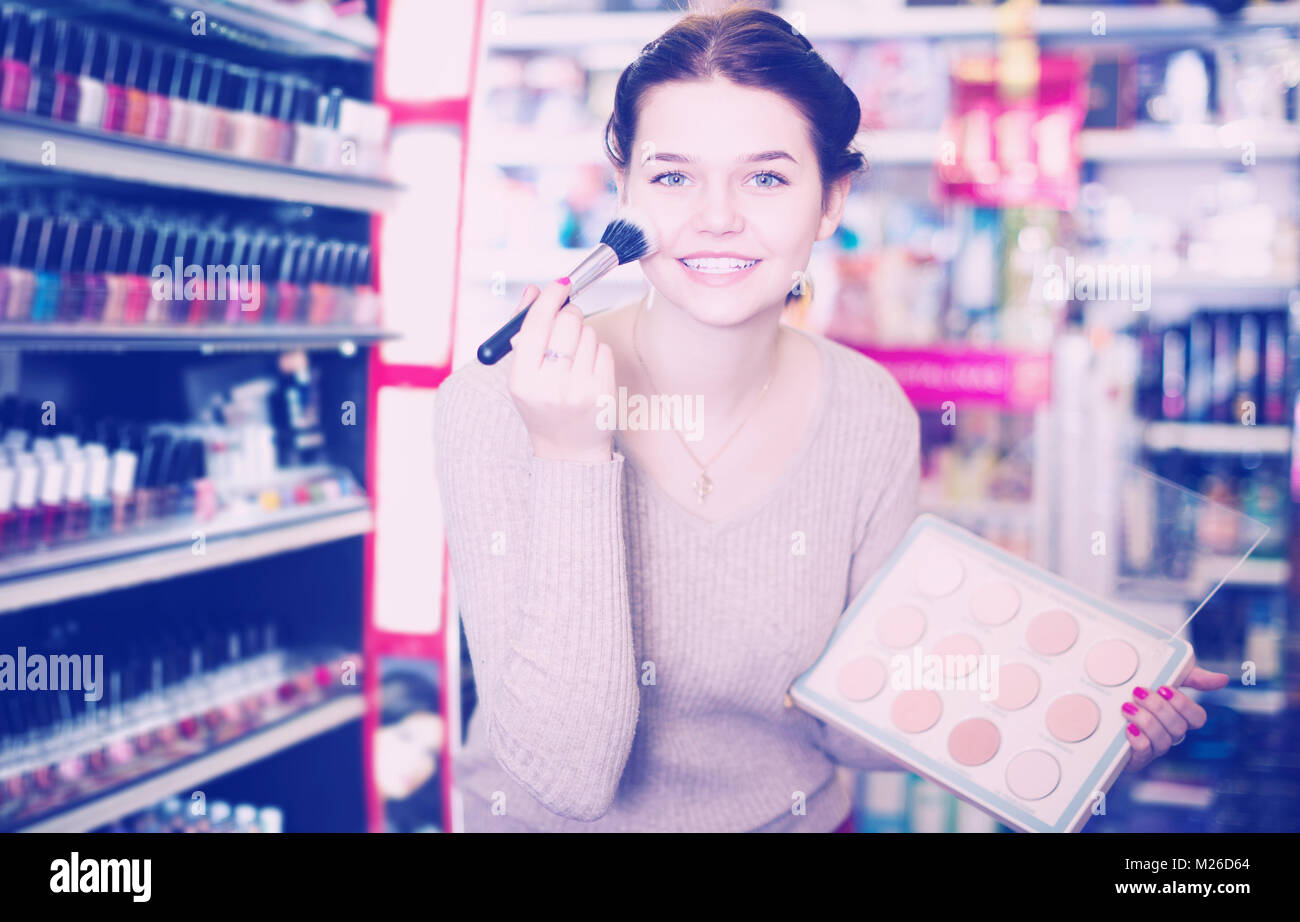 Smiling female customer looking for compact powder in cosmetics shop ...