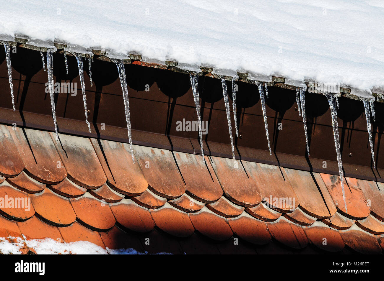 Long icicles hanging from snowy roof down to red roof panels at an old town house in Kaufbeuren, Bavaria Stock Photo