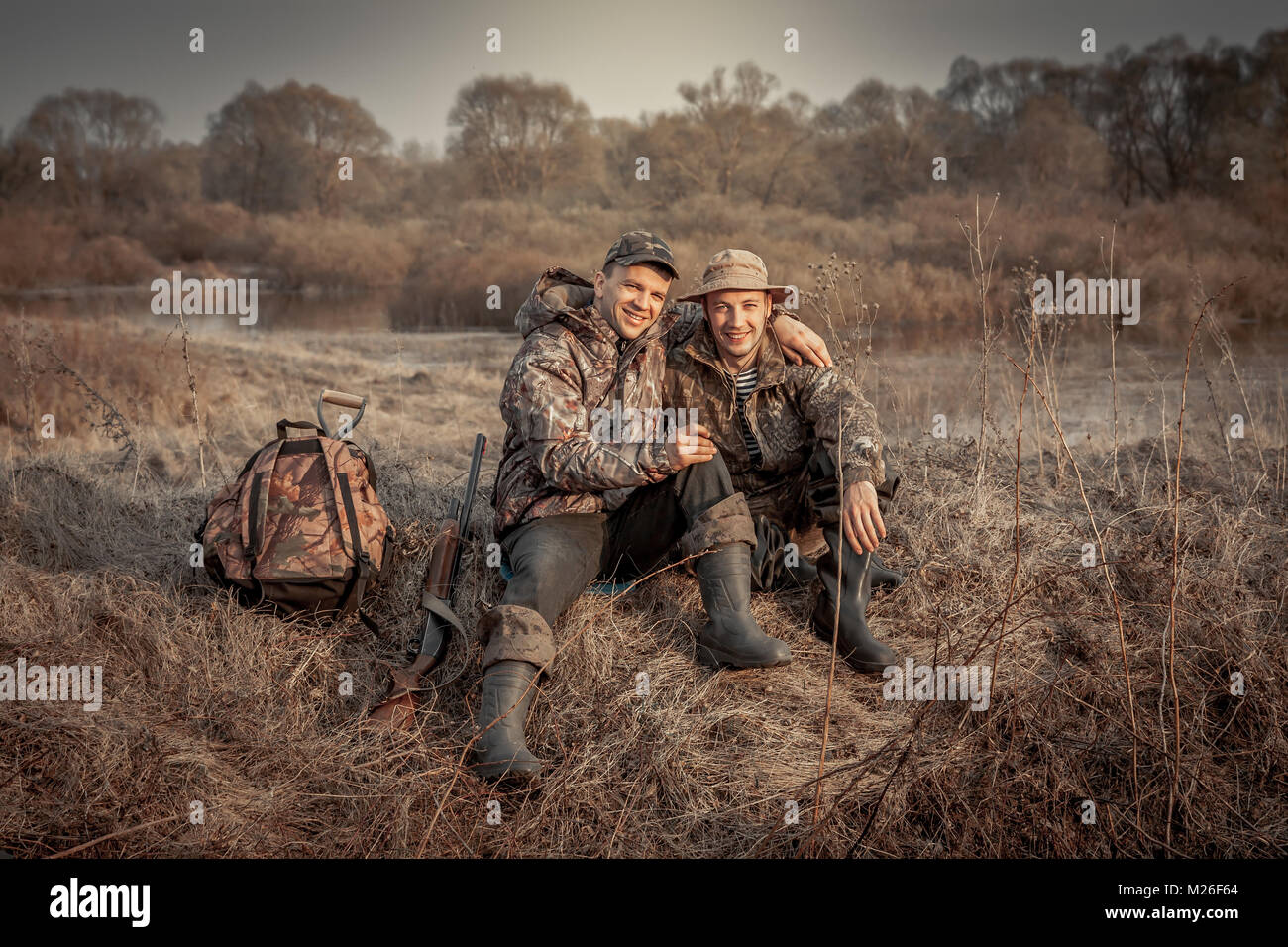 Hunter men friends resting in rural field during hunting period symbolizing strong friendship Stock Photo