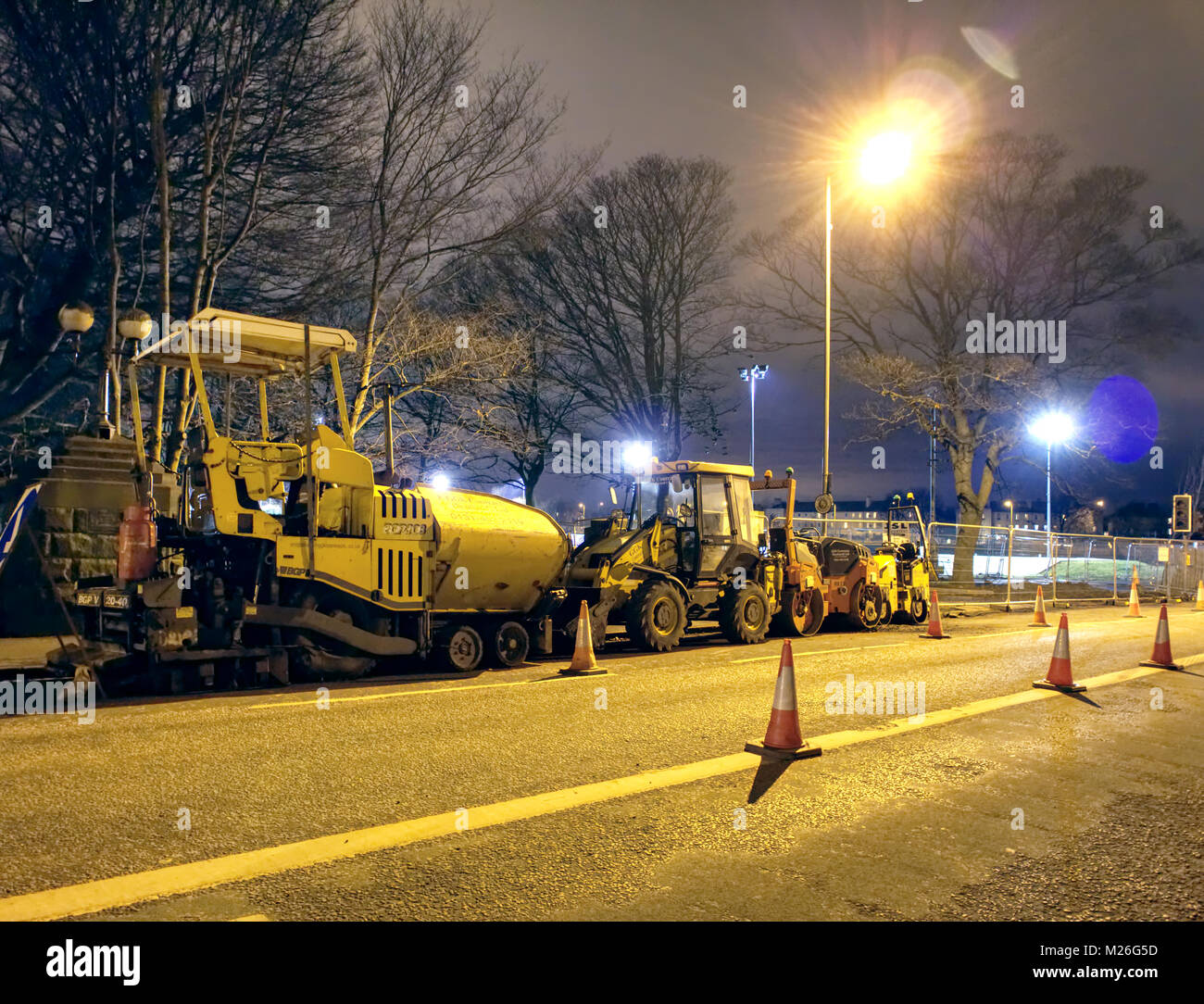 A raft of heavy road laying machine equipment on the side of the road at night in the suburbs of Edinburgh in winter. Stock Photo