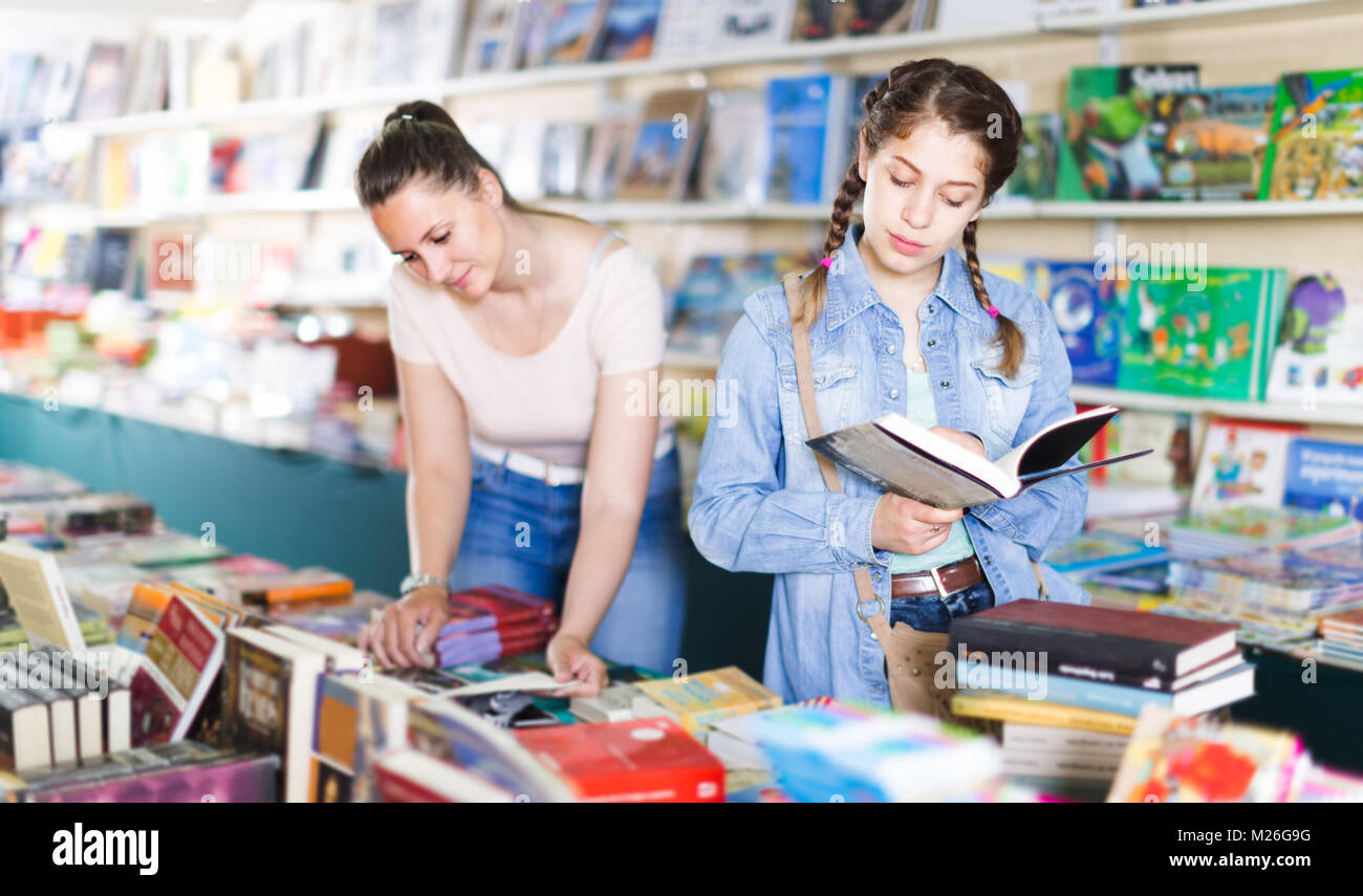 smiling happy woman showing open book to girl in school age in book boutique Stock Photo