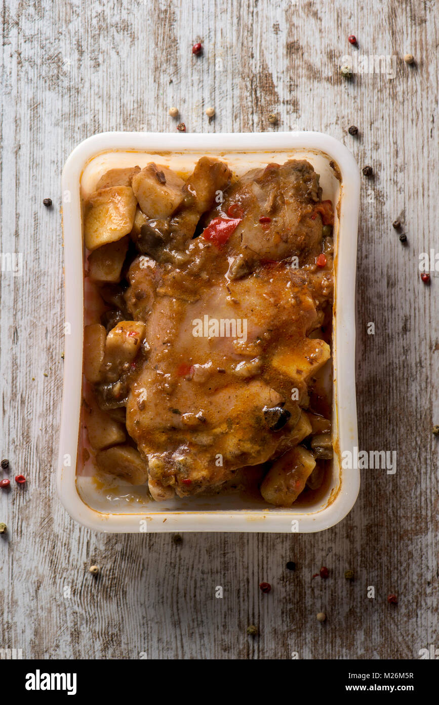 high angle view of a plastic container with manitas de cerdo, spanish stewed pigs trotters, on a white rustic wooden table Stock Photo