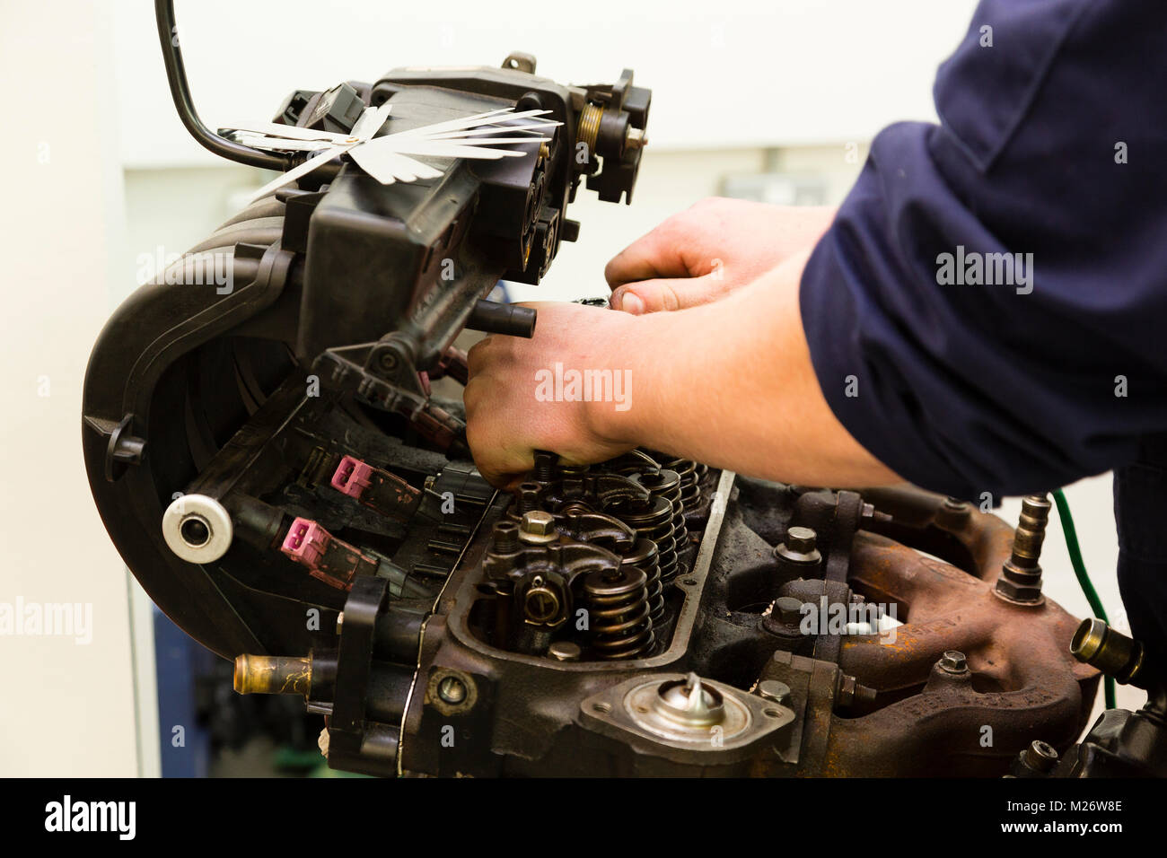 A young male apprentice works on a car engine while training to be a mechanic. Stock Photo