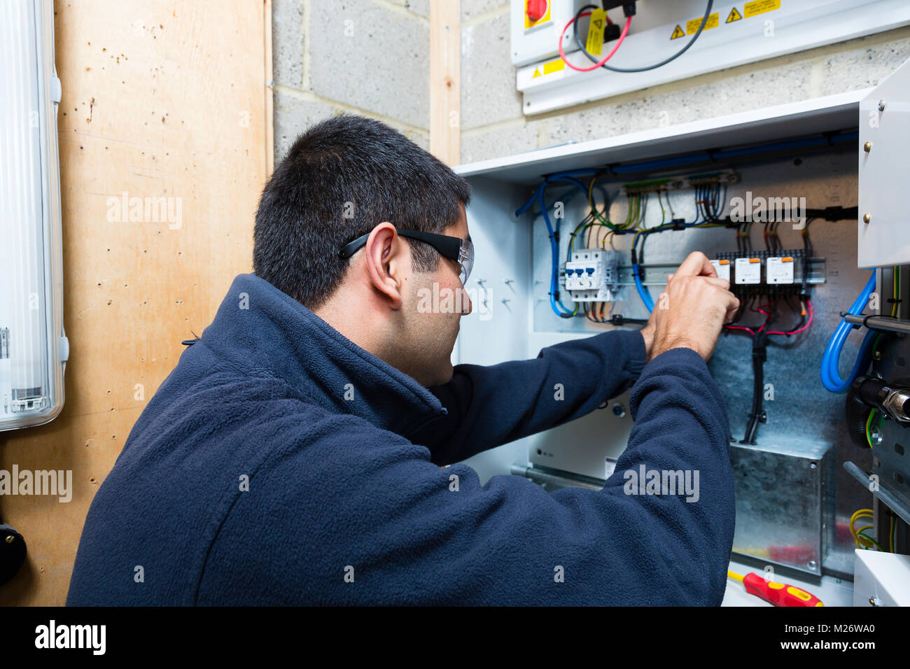 A young Asian apprentice electrician works with a screwdriver at a junction box. Stock Photo